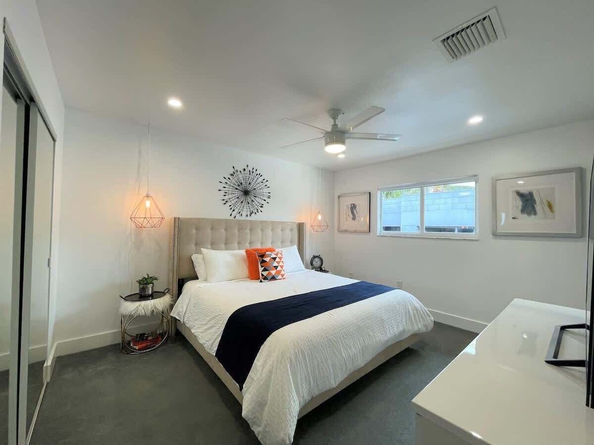 A modern bedroom with a large bed, bedside tables, a ceiling fan, and a window with a view.