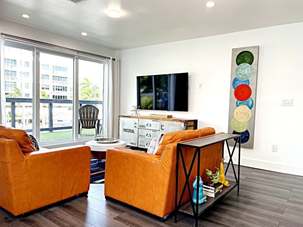A modern living room with two orange sofas, a wooden coffee table, and a TV on the wall.