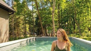 Ein Schwimmbad mit Holzterrasse und einem Haus im Hintergrund, umgeben von Bäumen.