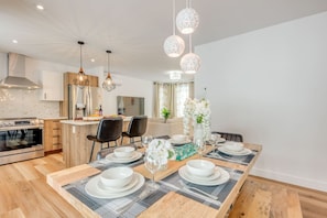Uma área de refeições moderna, com uma mesa de madeira posta para quatro pessoas, rodeada por cadeiras pretas.