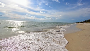 Une plage où les vagues viennent doucement lécher le rivage, un ciel dégagé et quelques personnes visibles au loin.