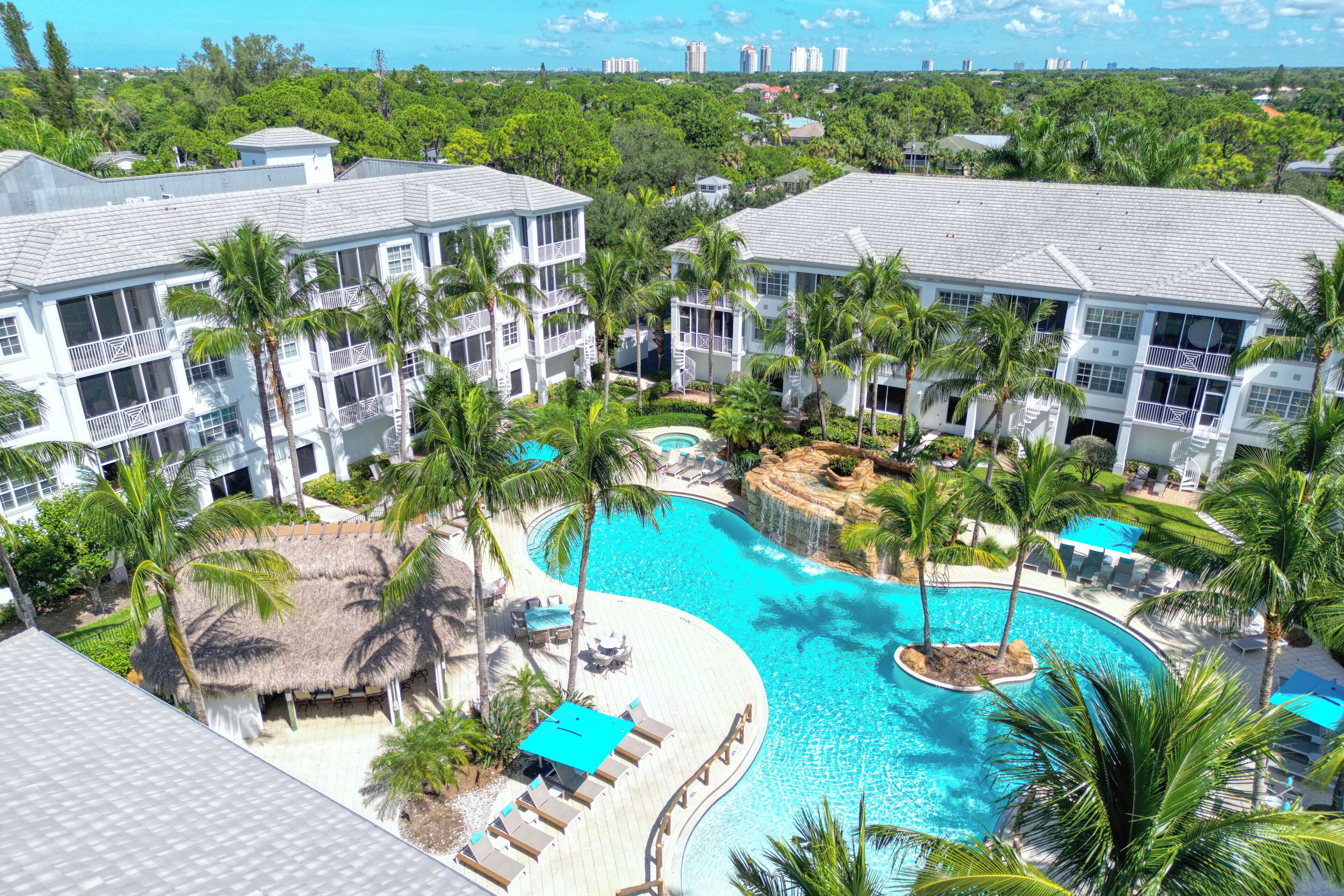 A resort with multiple buildings, a large swimming pool, and palm trees.
