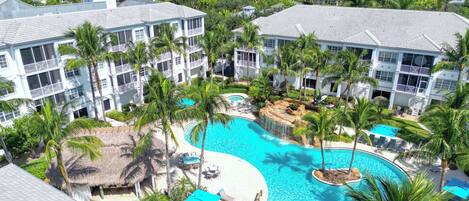 A resort with multiple buildings, a large swimming pool, and palm trees.