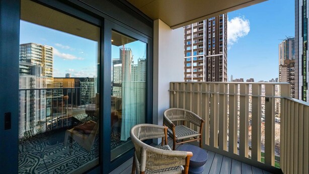 A balcony with two wicker chairs, a patterned rug, and a view of city buildings.