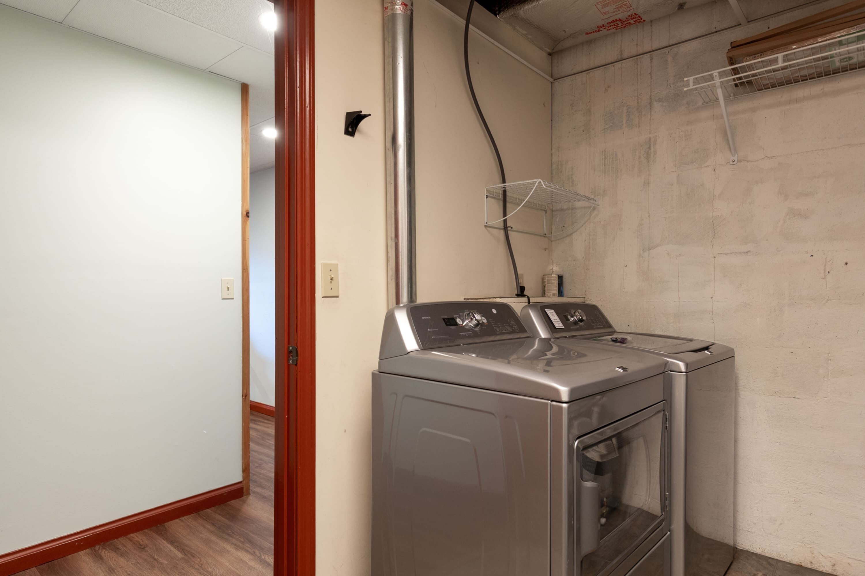 A laundry room with two stacked washers and dryers, a metal vent, and a white wall.
