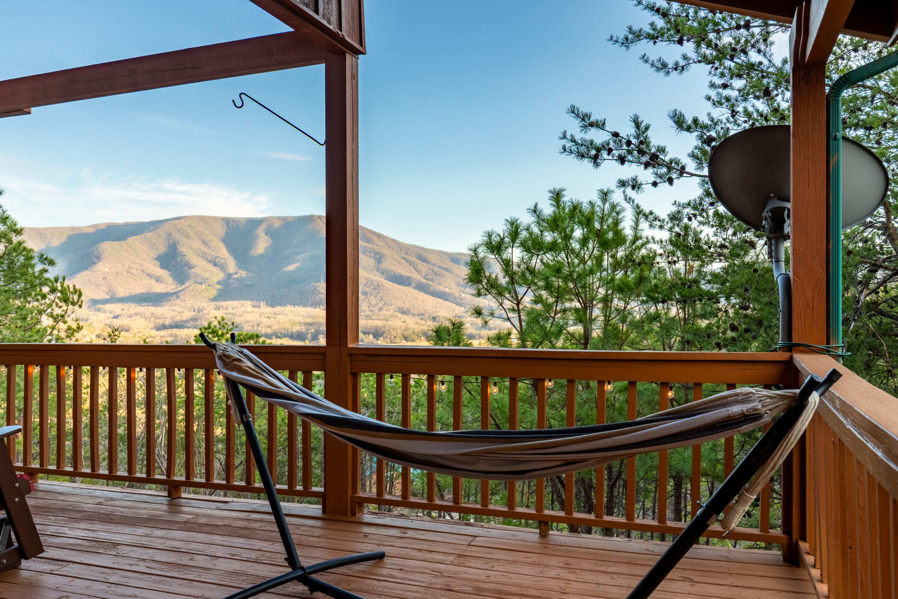 A wooden deck with a hammock, a satellite dish, and a view of mountains.