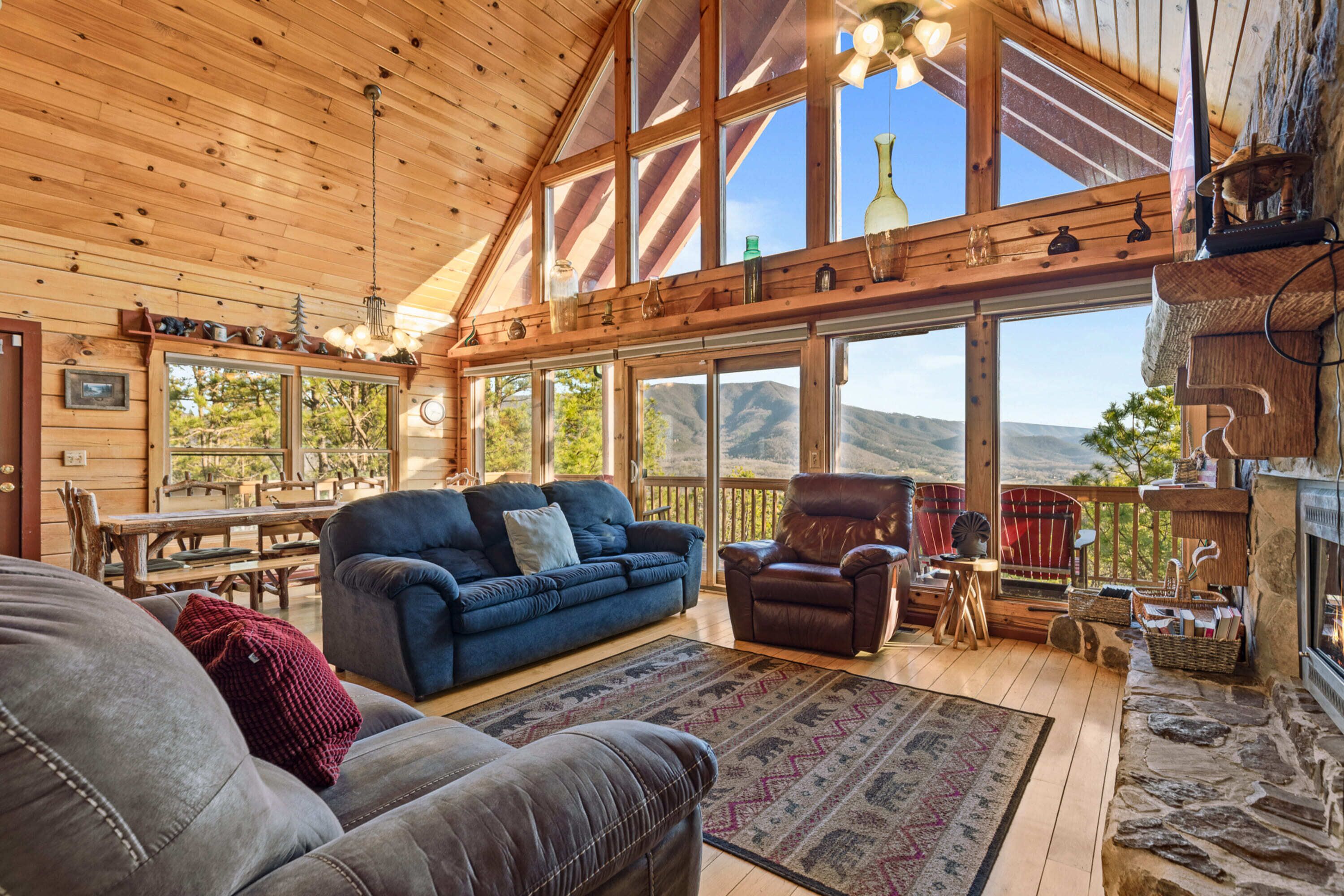 A spacious wooden cabin with a large living area featuring a blue sofa, leather armchairs, and a stone fireplace.