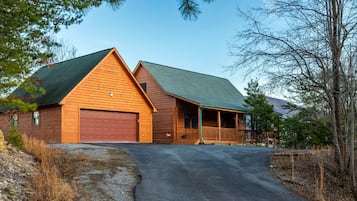 Cozy cabin with a covered porch and green roof, set amidst a natural landscape.