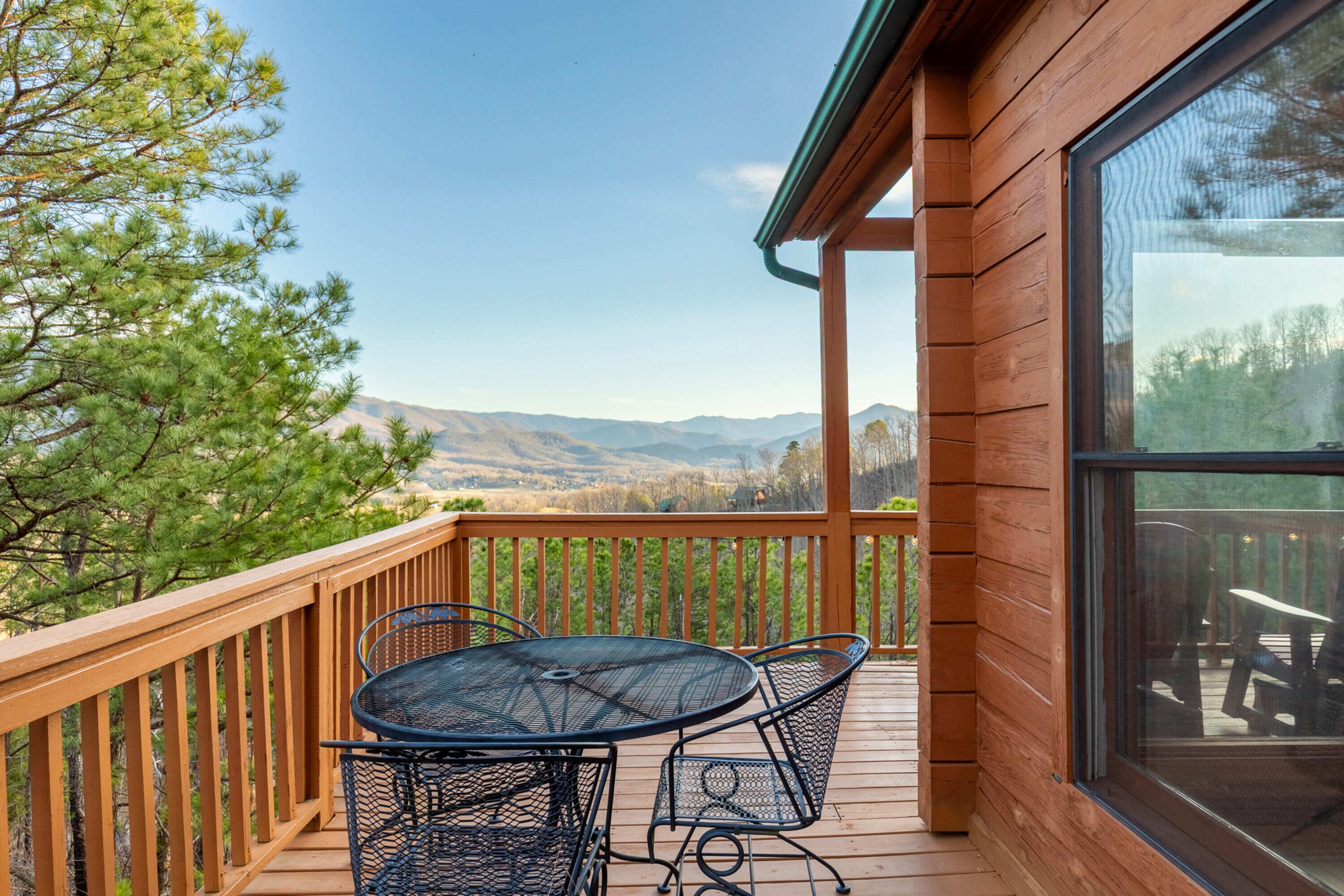 A wooden deck with a table and chairs, overlooking a mountainous landscape.
