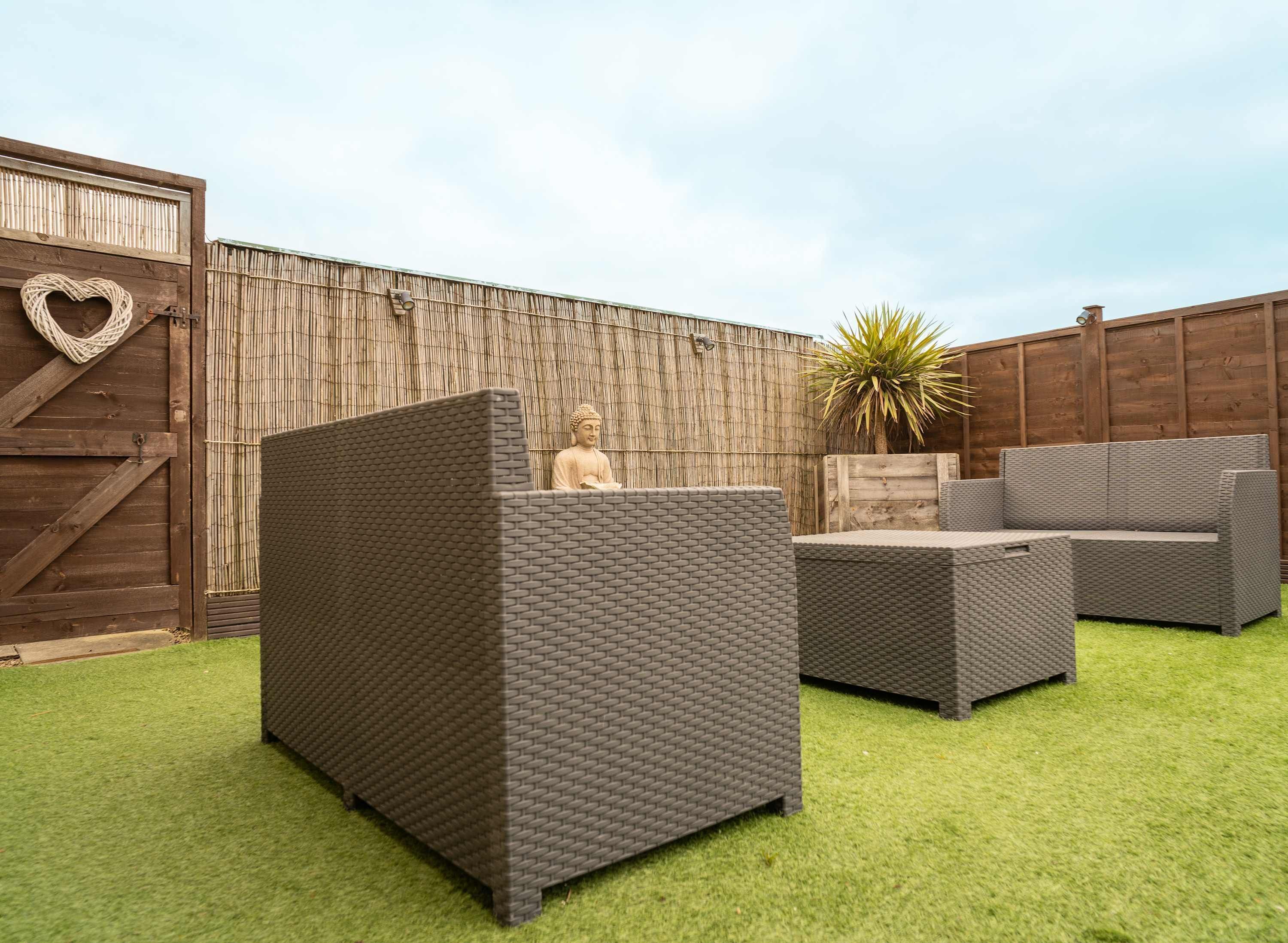 A patio area with a large woven sofa, a smaller sofa, and a heart-shaped decoration on a wooden wall.