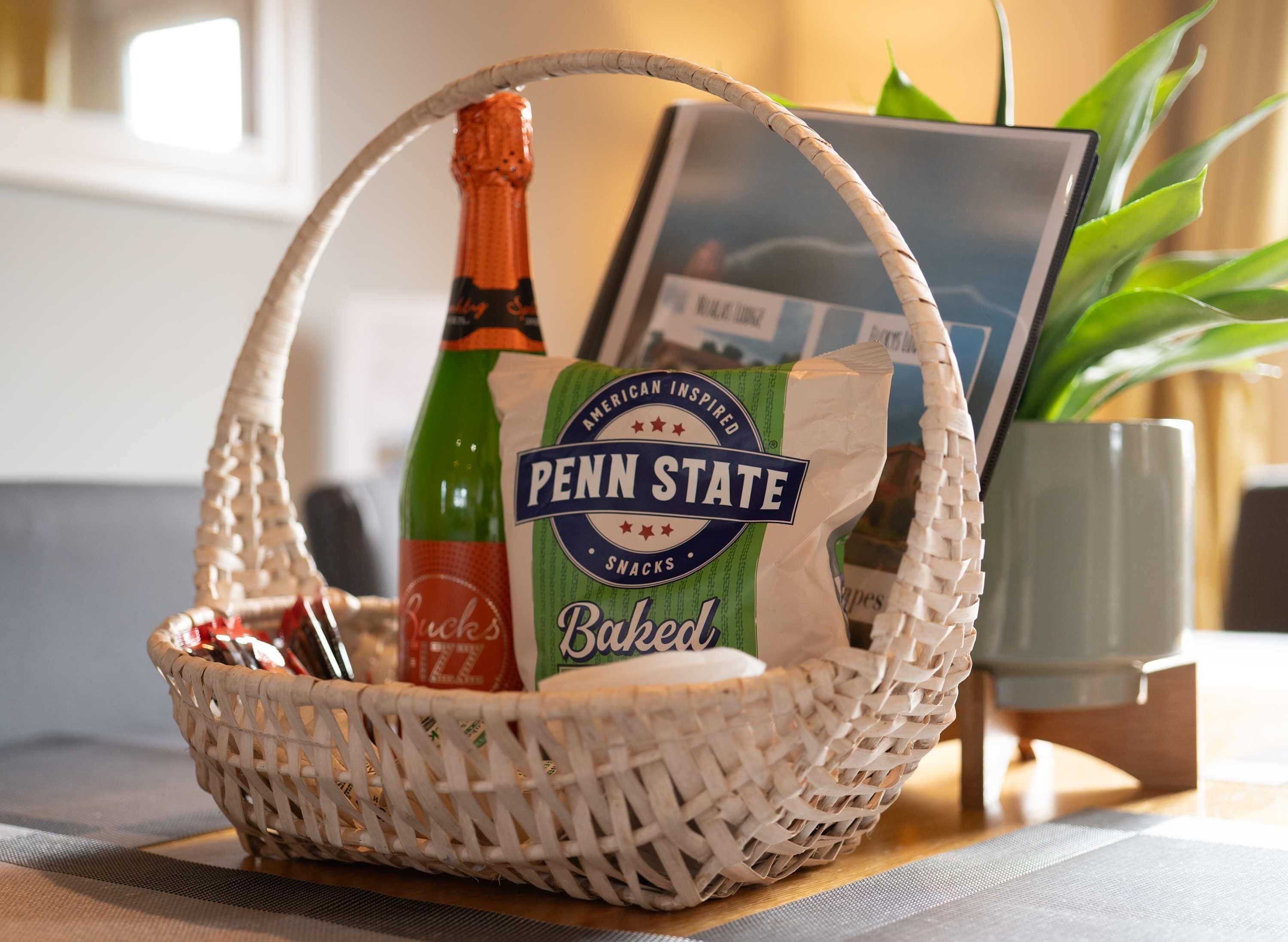 A woven basket containing a bottle of Buck's beer, a Penn State snacks bag, and a framed picture.