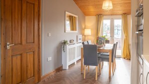 Une pièce avec une porte en bois, une table à manger avec des chaises, un radiateur blanc, un luminaire suspendu et une fenêtre avec des rideaux.