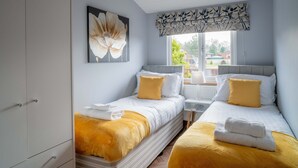 Une chambre avec deux lits, une grande fenêtre et un tableau représentant des fleurs.