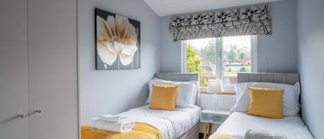 Une chambre avec deux lits, une grande fenêtre et un tableau représentant des fleurs.