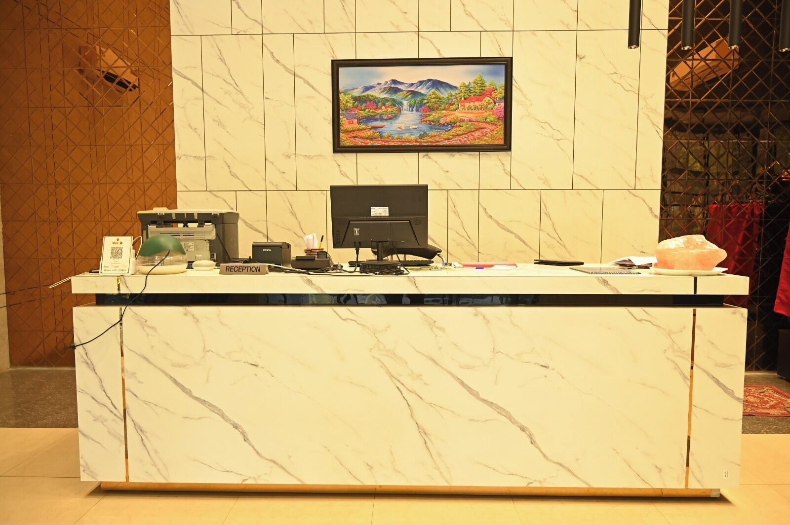 Mostrador de recepción con computadora, impresora y placa identificadora que dice 'RECEPTION'.