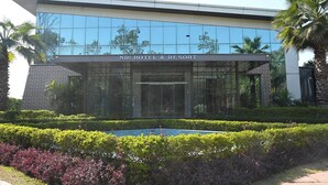 A modern hotel with a glass facade, a well-maintained garden, and a clear sign reading "NRI HOTEL & RESORT". - NRI Hotel (Barara)