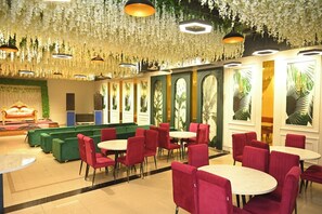 A hotel lobby with green sofas, red chairs, and round tables. - NRI Hotel (Barara)
