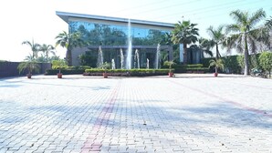 A modern hotel with a glass facade, a landscaped entrance with palm trees, and a paved driveway. - NRI Hotel (Barara)