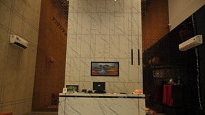 A reception desk with a marble wall, a painting, and air conditioning units. - NRI Hotel (Barara)