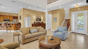 A spacious living area with a high ceiling, a kitchen with modern appliances, a staircase, and a dining area.