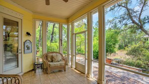 A covered porch with a wicker chair, a small table, and a view of the surrounding greenery.