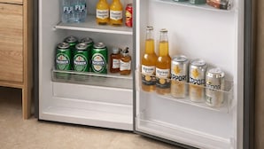 Een kleine koelkast met een magnetron erboven, gevuld met drankjes en snacks.