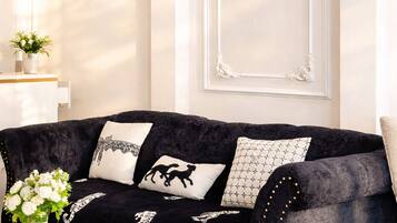 A dark velvet sofa with decorative pillows, a white marble coffee table, and a crystal chandelier.