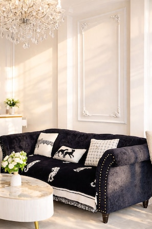 Un canapé en velours sombre agrémenté de coussins décoratifs, une table basse en marbre blanc et un lustre en cristal.
