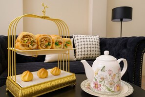 A dining setup with a gold-rimmed tray holding spring rolls and dumplings, a floral teapot, and a black floor lamp. - The Writeriana de Lumière (Ho Chi Minh City)