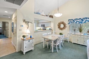 Une cuisine moderne avec des meubles blancs, une table à manger avec des chaises et un luminaire suspendu.