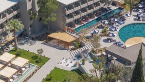 Et hotel med flere etager, udendørs swimmingpools og loungeområder med parasoller.