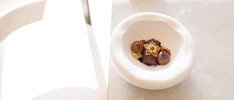 A white ceramic bowl with chocolate-covered treats and decorative elements on a marble surface.