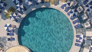 Oversigtsbillede af en cirkelformet swimmingpool omgivet af liggestole og parasoller.