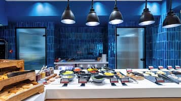 A buffet with various food items and name tags, set against a blue-tiled wall with hanging pendant lights.