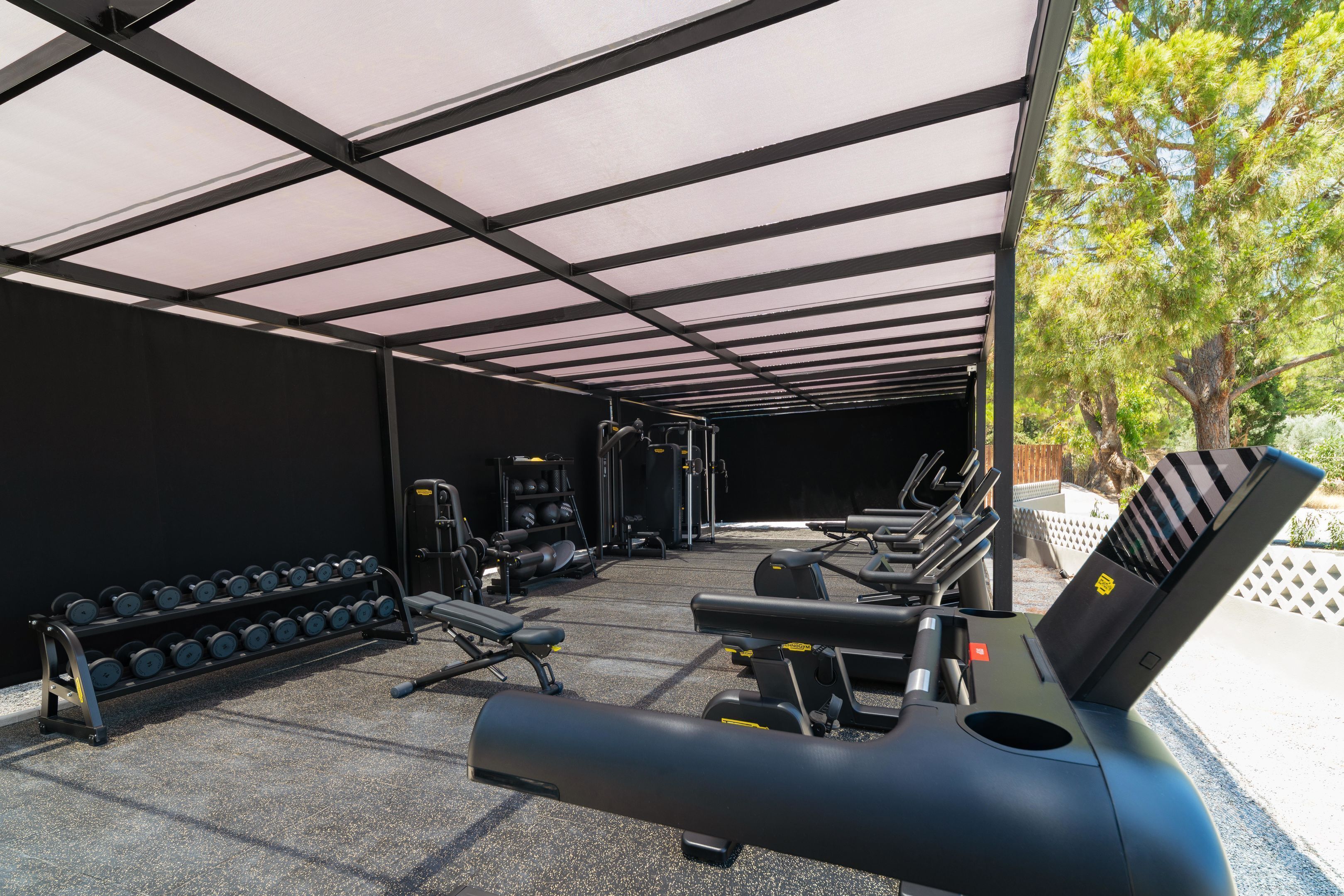 A covered outdoor gym area with exercise equipment, including treadmills and dumbbells.