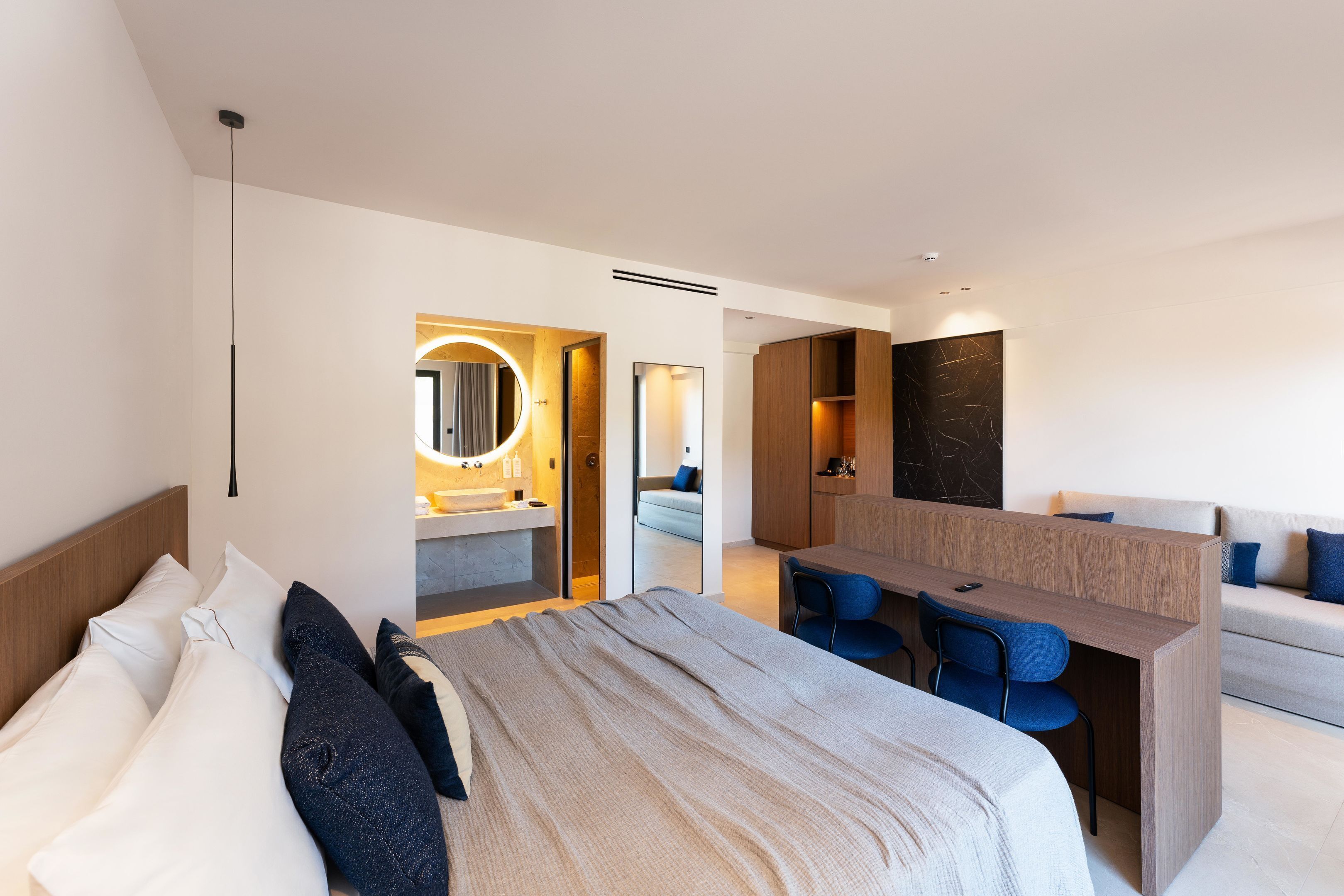 A modern hotel room with a bed, a desk, a sofa, and a bathroom.