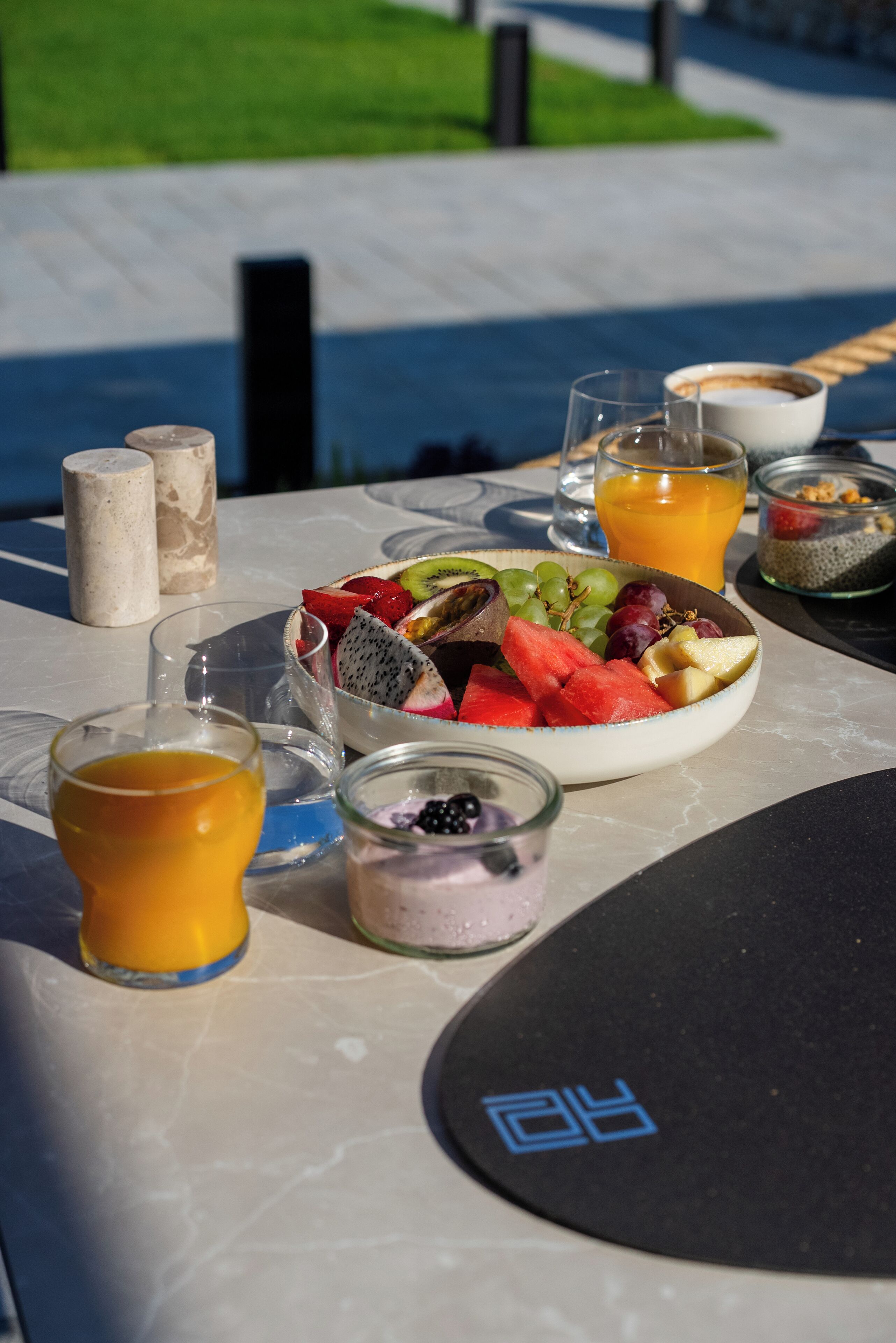 A table set with a fruit bowl, glasses of orange juice, a bowl of yogurt, and a glass of water.
