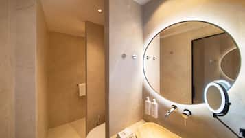 Un baño moderno con piso de mármol, inodoro independiente, lavamanos con recipiente de mármol y un espejo grande con luz circular.