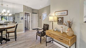 A dining area with a wooden table and chairs, a wooden console table with decorative items, and a wall-mounted lamp. - 52 Ocean Breeze: Free Bikes, Tennis & Pool, Pet Friendly! (Hilton Head Island)