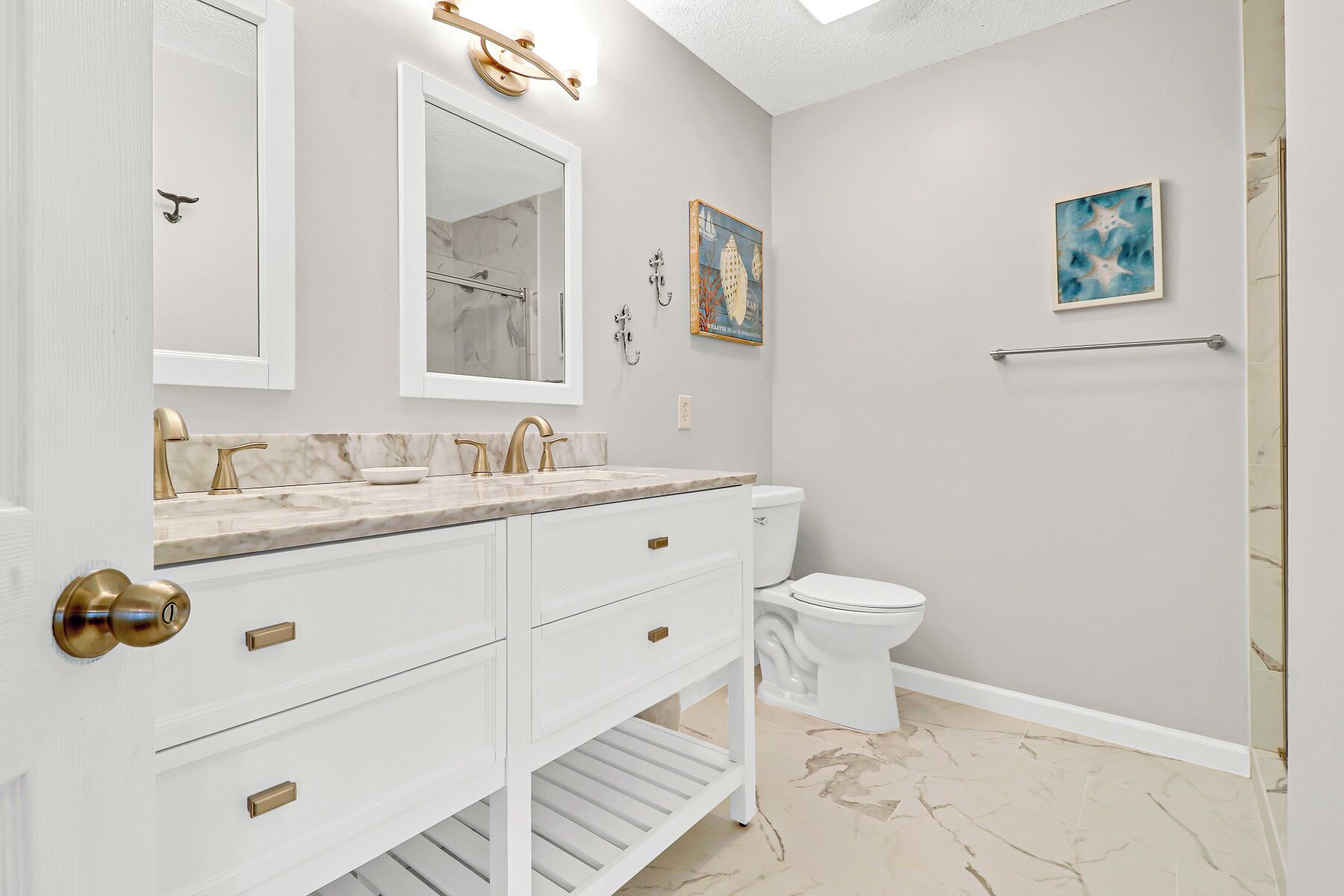 Une salle de bain avec un meuble-lavabo blanc, des robinetteries dorées, un plan de toilette en marbre, des toilettes et un espace douche.