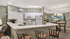 A modern kitchen with white cabinets, a central island with bar stools, a refrigerator, and a microwave. - 52 Ocean Breeze: Free Bikes, Tennis & Pool, Pet Friendly! (Hilton Head Island)