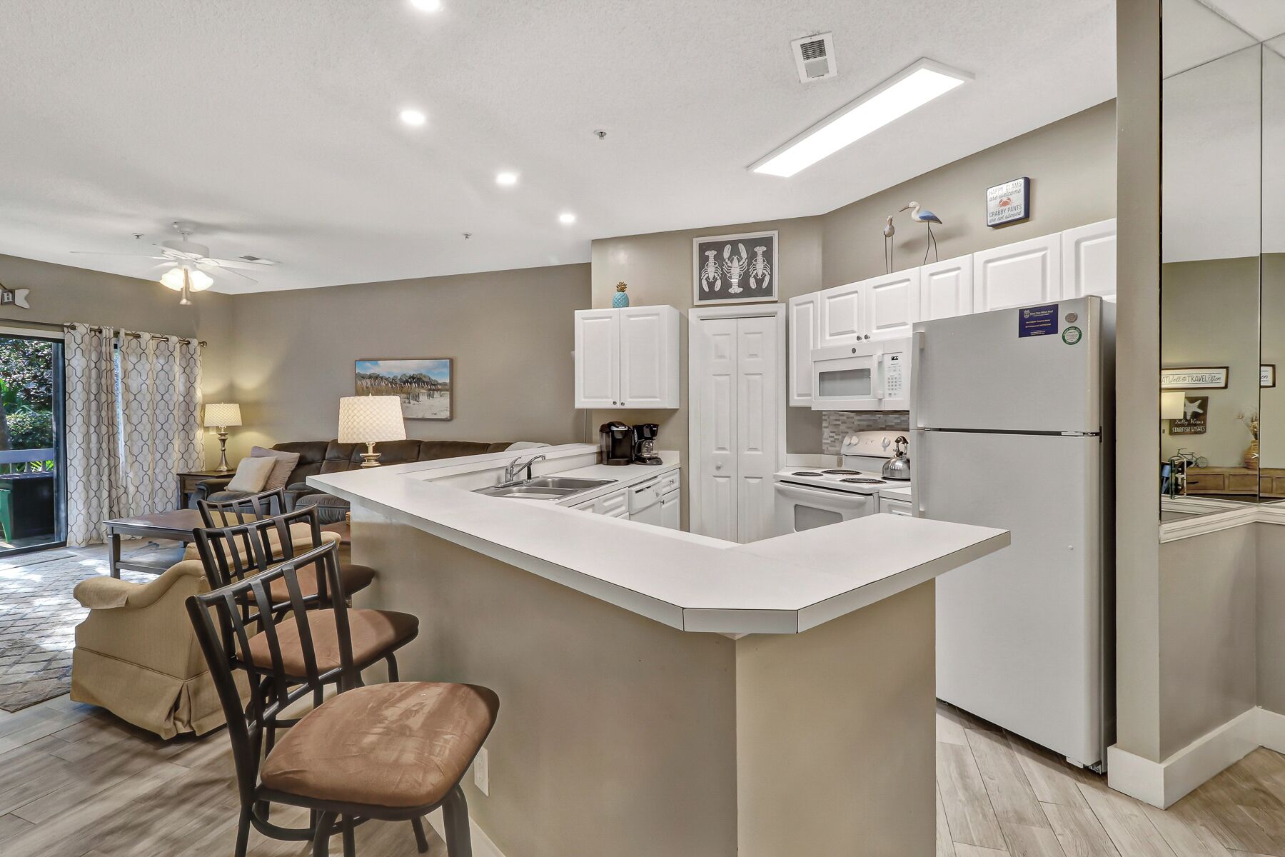 A modern kitchen with a central island, white cabinetry, and a dining area with a sofa and chairs.