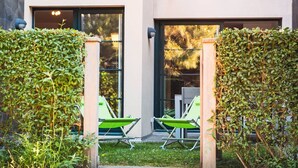 A modern building with two large glass doors, a small lawn, and two green lounge chairs.
