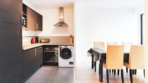 A modern kitchen with dark cabinetry, a built-in oven, a microwave, and a dishwasher. There is a dining area with a table and chairs.