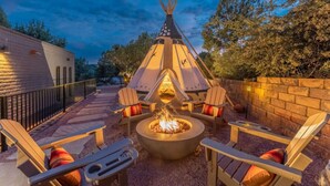 Un espacio al aire libre con tiendas de estilo teepee, una fogata, sillas Adirondack y un muro de piedra.