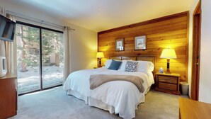 Une chambre avec un grand lit, deux lampes de chevet, une tête de lit en bois et une porte-fenêtre coulissante donnant sur un espace extérieur enneigé.
