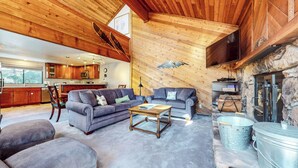 Un vaste espace de vie doté d’un plafond haut et de poutres en bois, comprenant deux canapés, une table basse et une cheminée en pierre.