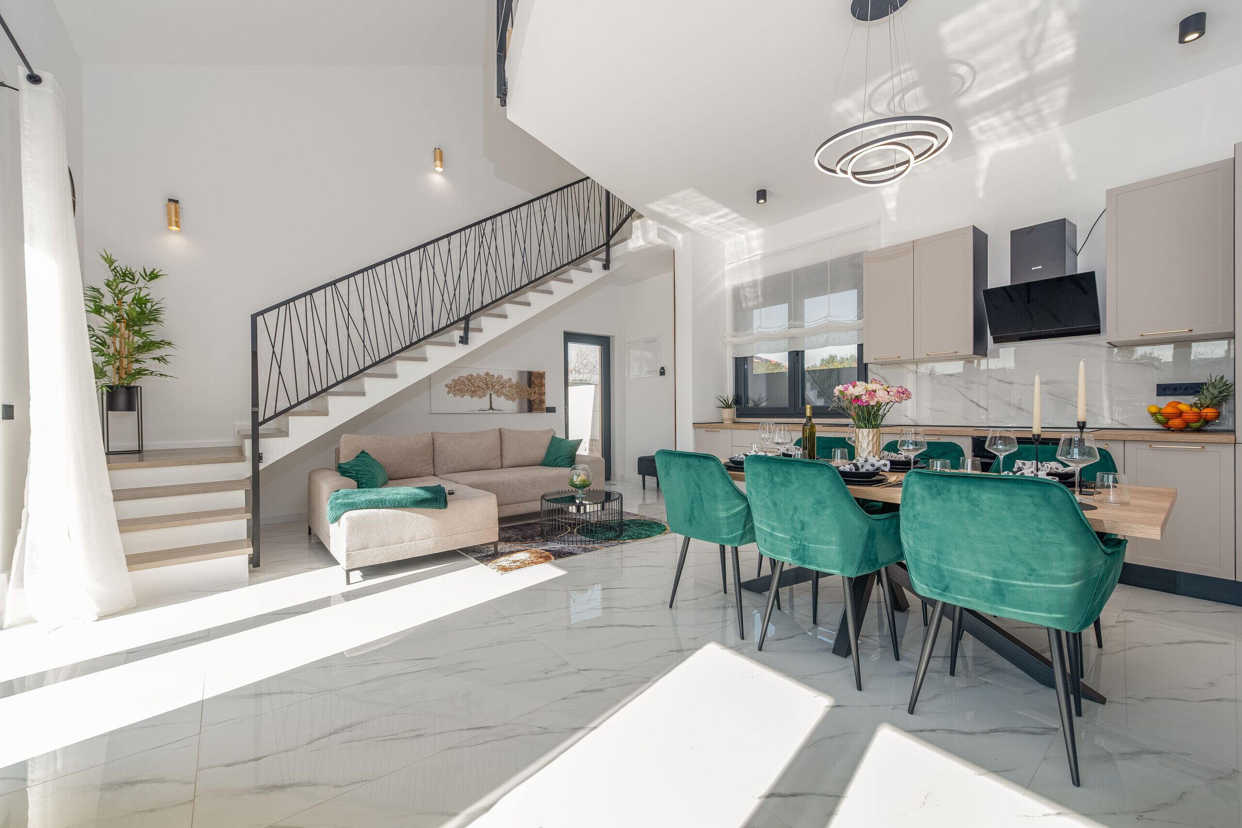 Amplia sala de estar con una escalera, un comedor con sillas verdes y una cocina con televisor de pantalla plana.