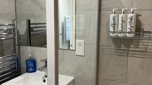 Un bagno con un lavandino bianco, una cabina doccia in vetro e articoli da toilette su un ripiano.