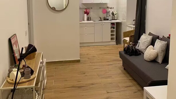 A modern apartment with a wooden floor, a dark sofa, a small table, and a kitchen in the background. - Bocca di rosa in centro (La Spezia)